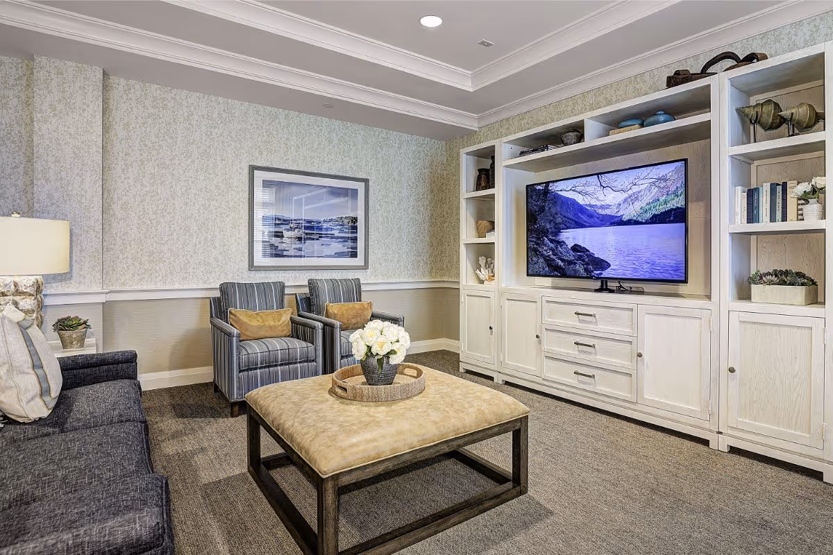 Comfortable living room with sofa and armchairs centered around an ottoman and a built-in entertainment center with a TV.
