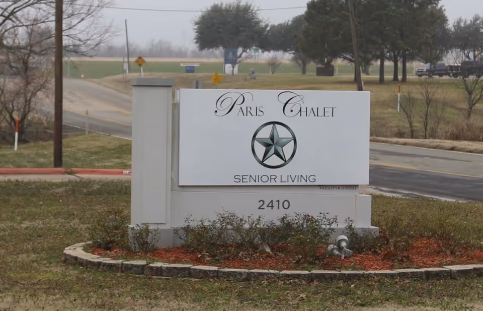 Entrance sign reading "Paris Chalet Senior Living" with the address 2410 on a grassy roadside median.