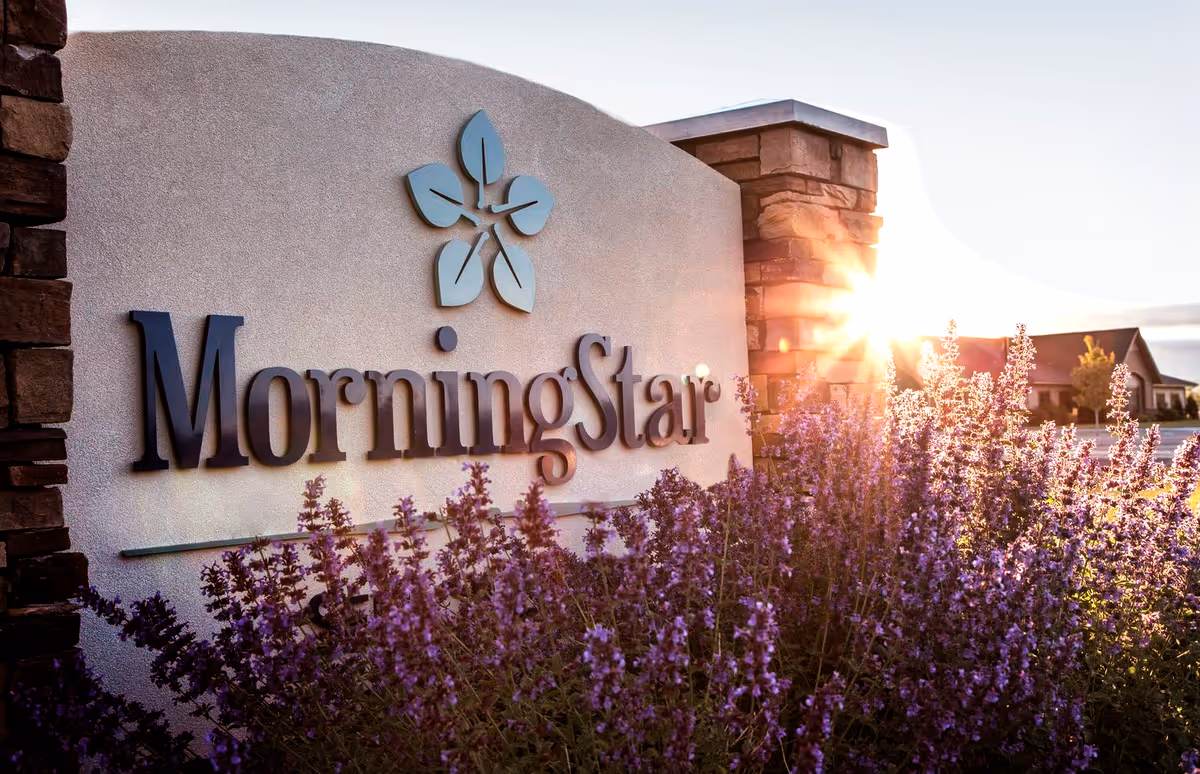 Entrance sign reading 'MorningStar' with a floral logo, stone pillars, and purple flowers in front lit by the rising sun.
