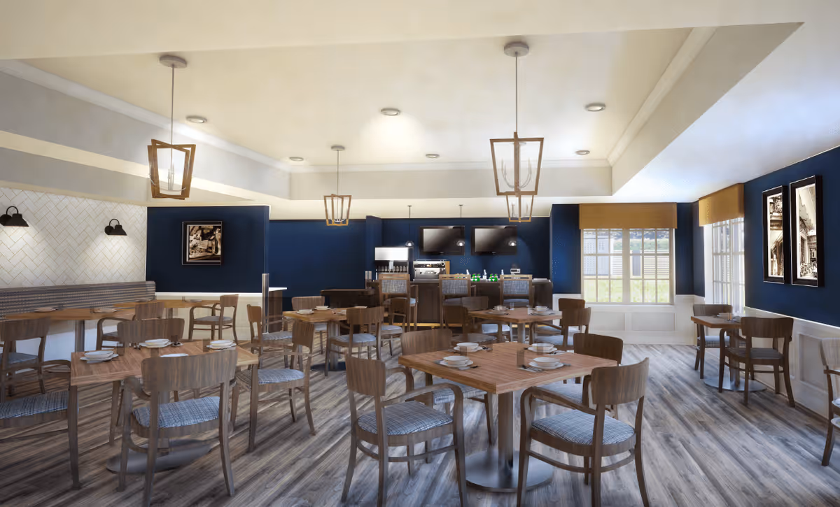 A spacious dining room with multiple wooden tables and chairs arranged neatly. Each table is set with plates and bowls. The room features dark blue walls with white wainscoting, large windows with beige blinds allowing natural light, and modern pendant lights hanging from the ceiling. There is a counter area with two televisions mounted on the wall and beverage dispensers behind it.