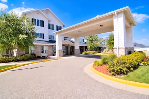 Wide view of Oakwood Hills Sky Active Living facility entrance with covered driveway and landscaping.