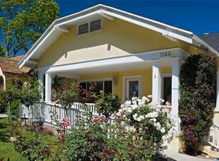 A single-story pale-yellow senior living facility with a white front porch and rose garden.