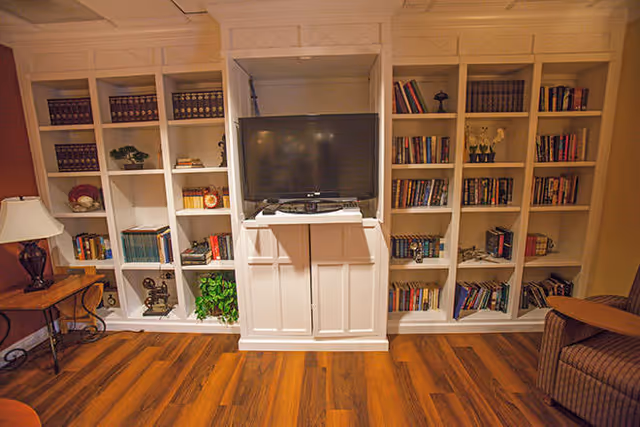 White built-in bookshelves filled with books and décor surround a central cabinet holding a TV in a cozy room with hardwood floors.
