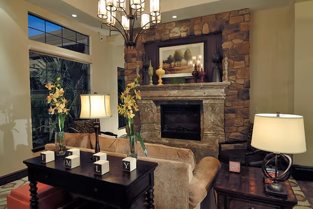 Cozy living room with a stone fireplace, sofa, side tables with lamps, decorative vases, and a chandelier.