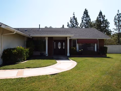 Single-story senior living facility exterior with curved walkway to entrance and manicured lawn.