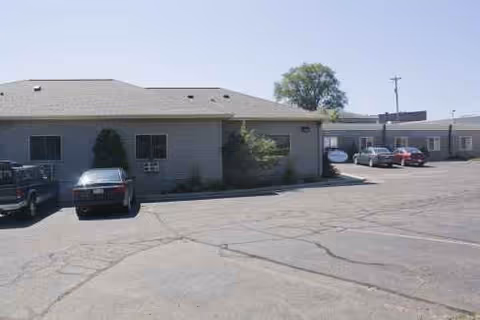 Exterior view of a single-story facility with a parking lot and several cars.