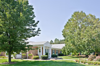 Single-story brick building with a white portico entrance set among trees and a manicured lawn.