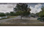 Front exterior view of a facility lot with a tree, road, and distant building