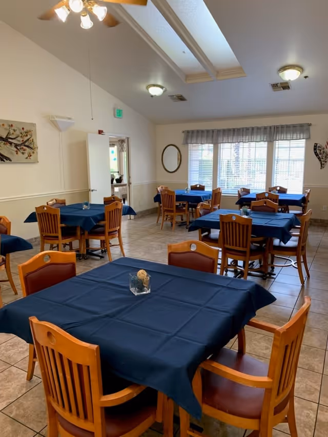 Dining room with multiple square tables covered in dark blue tablecloths and wooden chairs beneath skylights and ceiling fans.