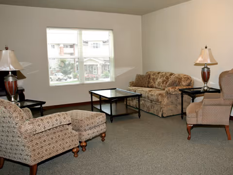 Neutral living room with patterned sofa and armchairs around a glass-top coffee table beneath a large window.