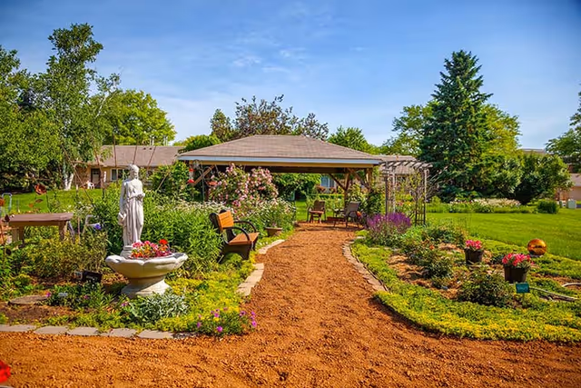 Garden path leading to a gazebo surrounded by flowerbeds, benches, and a statue.