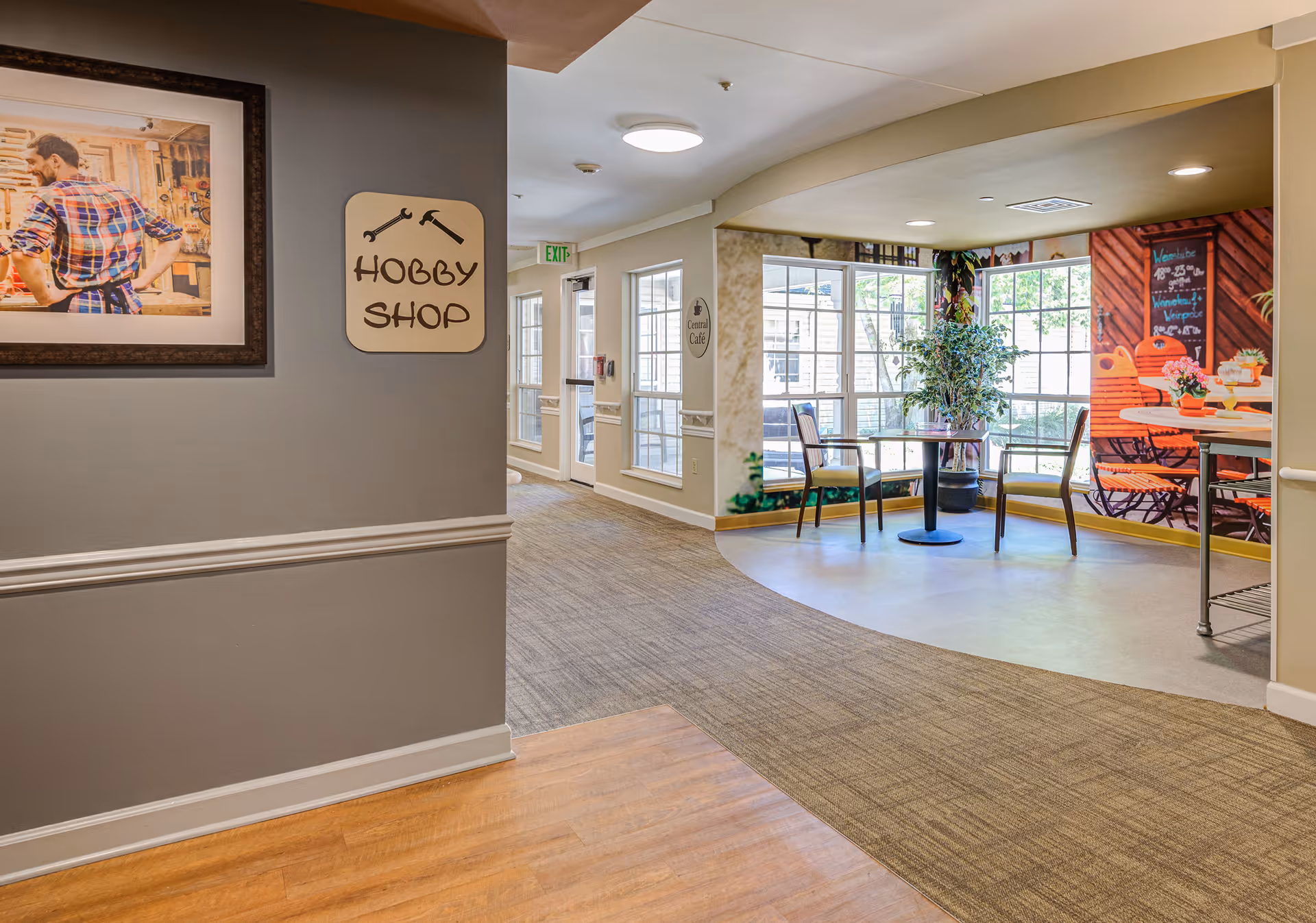 A bright interior hallway and seating area with a 'Hobby Shop' sign on the wall and table-and-chairs by large windows.
