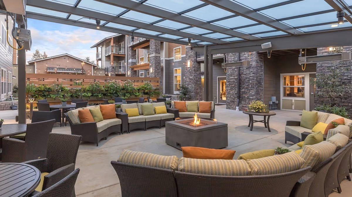 Covered outdoor courtyard with curved wicker seating and a central fire pit in a senior living community.