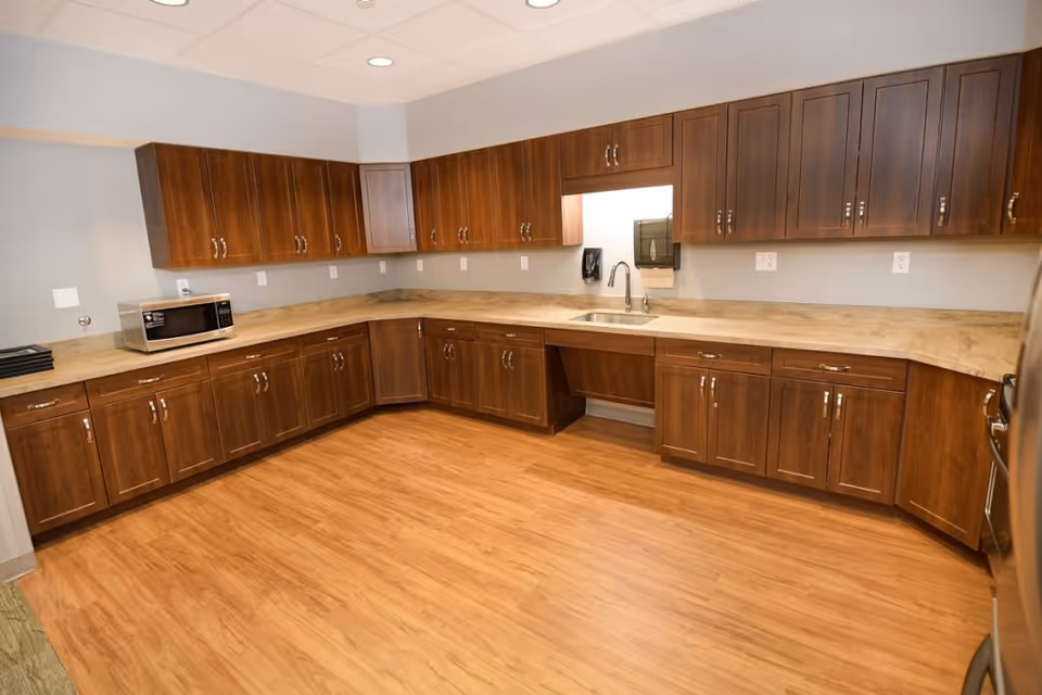 Spacious kitchen with L-shaped wooden cabinets, a sink, countertop, microwave and wood-look flooring.