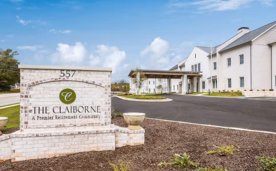 Entrance sign reading "The Claiborne A Premier Retirement Community" in front of the facility's white brick building and covered drive-up.