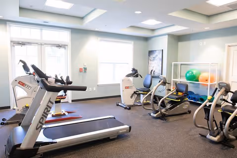 Bright fitness room with treadmills, recumbent bikes, exercise balls and mats in a senior living community.