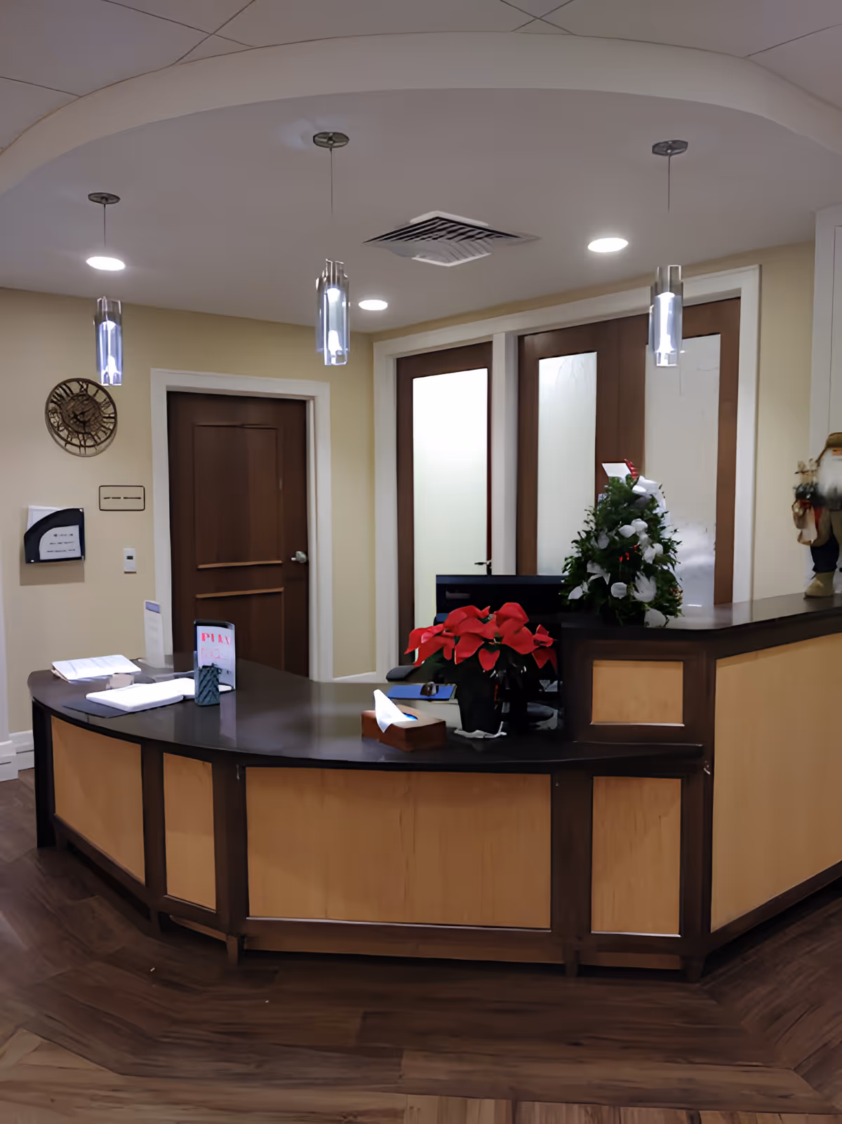 Curved wooden reception desk in a facility lobby with pendant lights, poinsettia and holiday decorations.