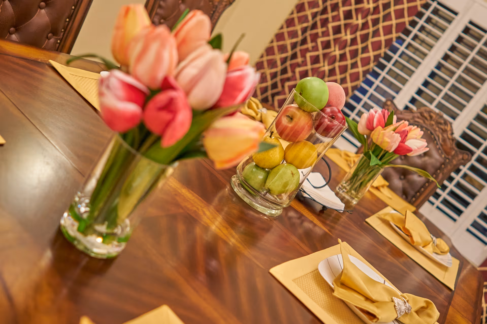 A formal dining table set with tulip bouquets and a glass vase filled with apples as a centerpiece.