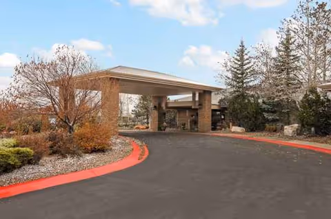 Wide driveway leads to a covered entrance of Life Care Center of Cheyenne with landscaping.
