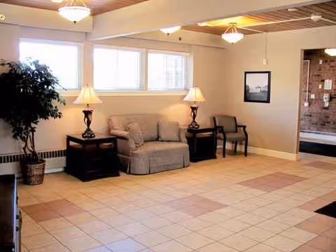 Lounge area with sofa, armchairs, lamps, and a potted plant along a tiled floor.