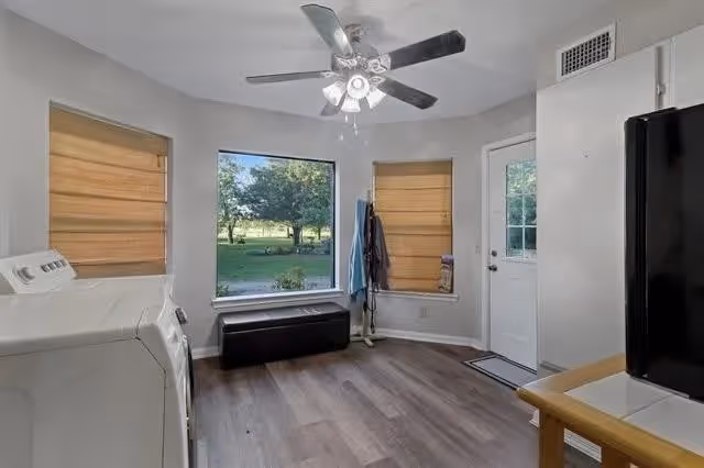 Utility/mudroom with a washer and dryer on the left, a refrigerator and counter on the right, a bench under a large window, and a door to the outside.