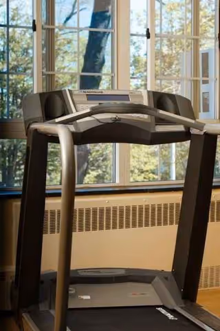 Treadmill in a well-lit indoor exercise room with large windows.