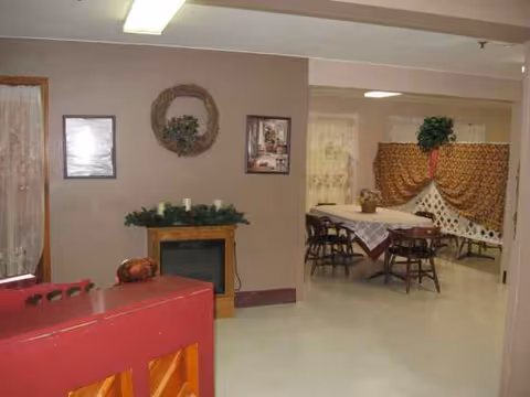 Interior of a senior living facility showing a dining area with tables, chairs, and decorations.
