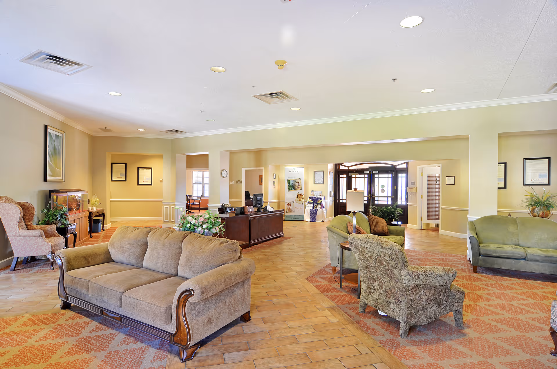 Well-lit communal lobby with sofas, armchairs, a reception desk, and entry doors in the background.