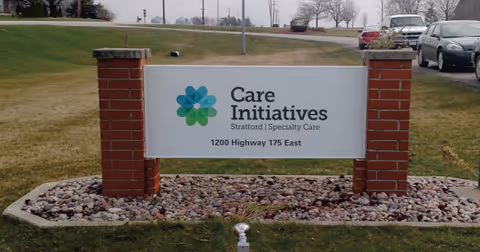 Outdoor sign mounted between two brick posts on a lawn reading 'Care Initiatives Stratford | Specialty Care 1200 Highway 175 East'.