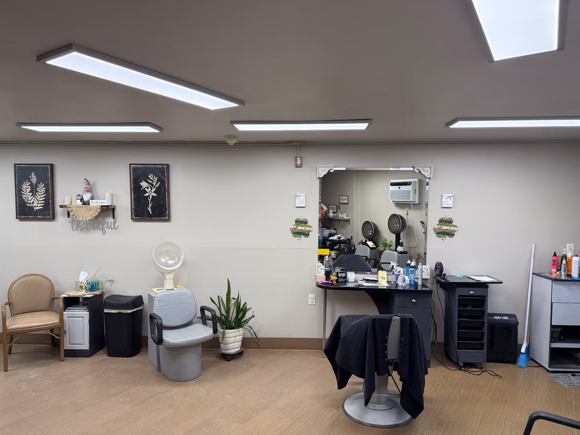 Interior view of a small salon area with styling chairs, mirrors, a hood dryer, waiting chairs and salon supplies.