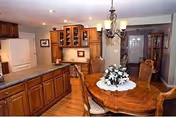 Open-plan kitchen and dining area with wooden cabinets, a central island, and a round dining table with a floral centerpiece.