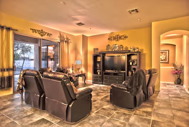 Spacious living room with leather recliner seating arranged around a TV entertainment center and sliding glass doors to the outside.