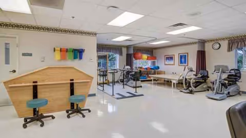 Bright rehabilitation gym interior with exercise equipment, therapy mats, and seating.