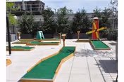 Miniature golf putting course on a tiled outdoor patio with several greens and a red windmill obstacle.