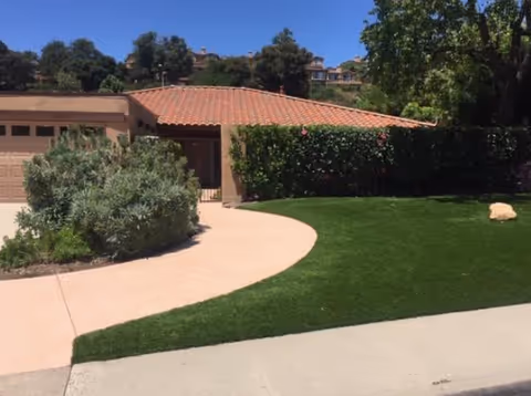 Exterior view of Sunset Homes showing a curved walkway, green lawn, and surrounding hedges.