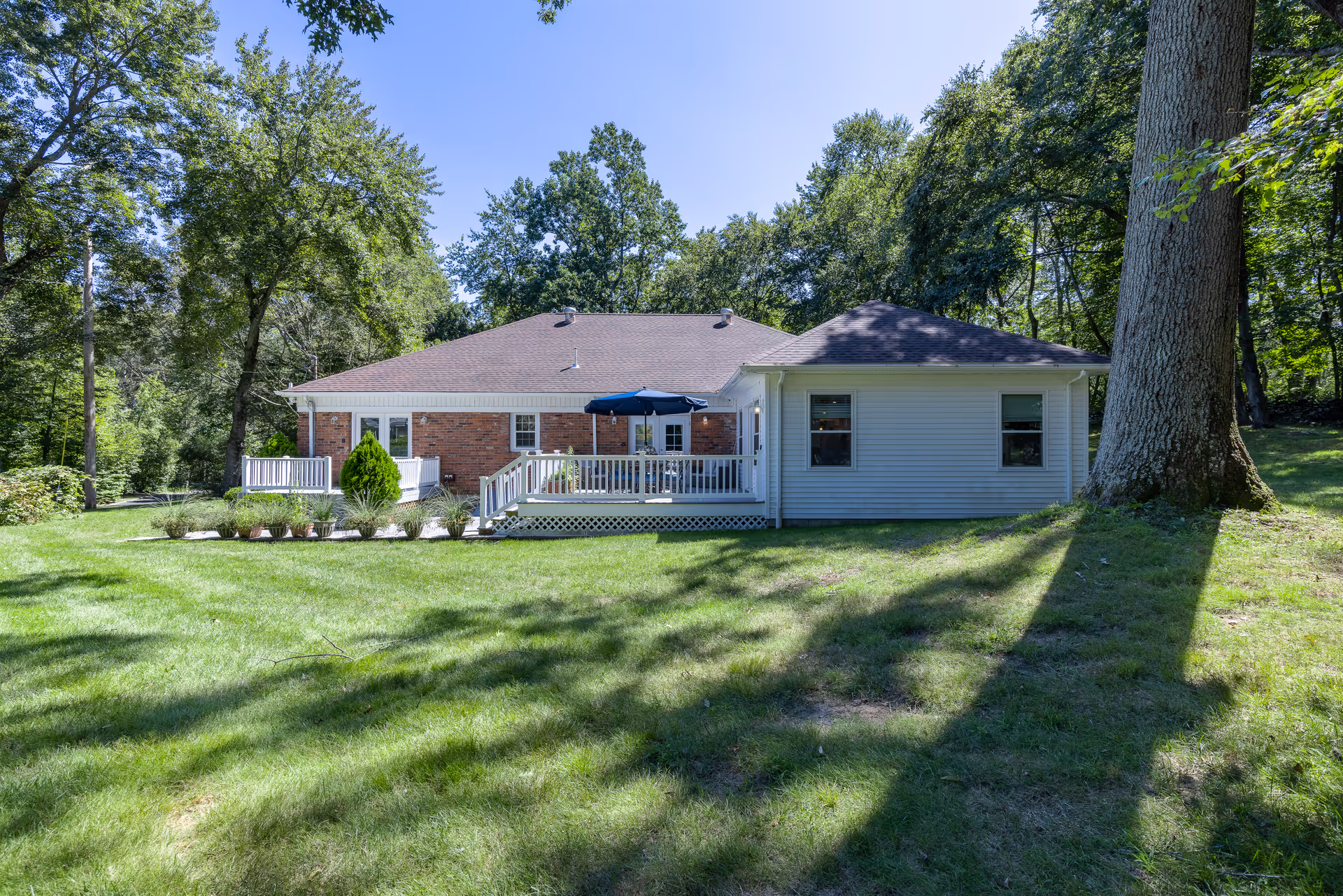 Single-story house with brick and light siding, white deck, and surrounding green lawn.