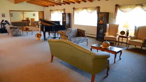 Spacious lounge with upholstered sofas and chairs, a grand piano, exposed wooden beams, and large windows.