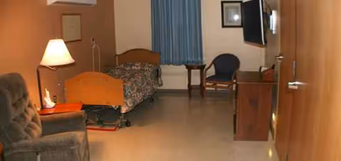 A furnished senior living facility bedroom with a bed, seating, and a window.