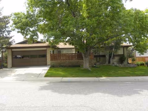Front view of a single-story assisted living facility with a garage, tree, and lawn.