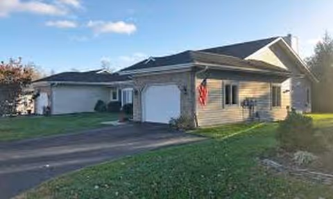 A single-story beige house with two garages, a driveway, and a manicured lawn.