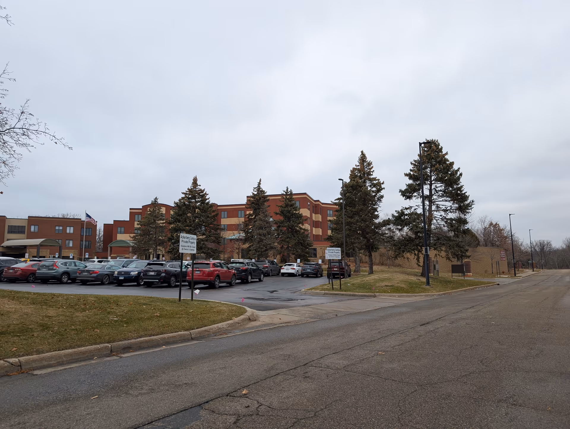 Exterior view of a multi-story senior living facility with parked cars and trees under an overcast sky.