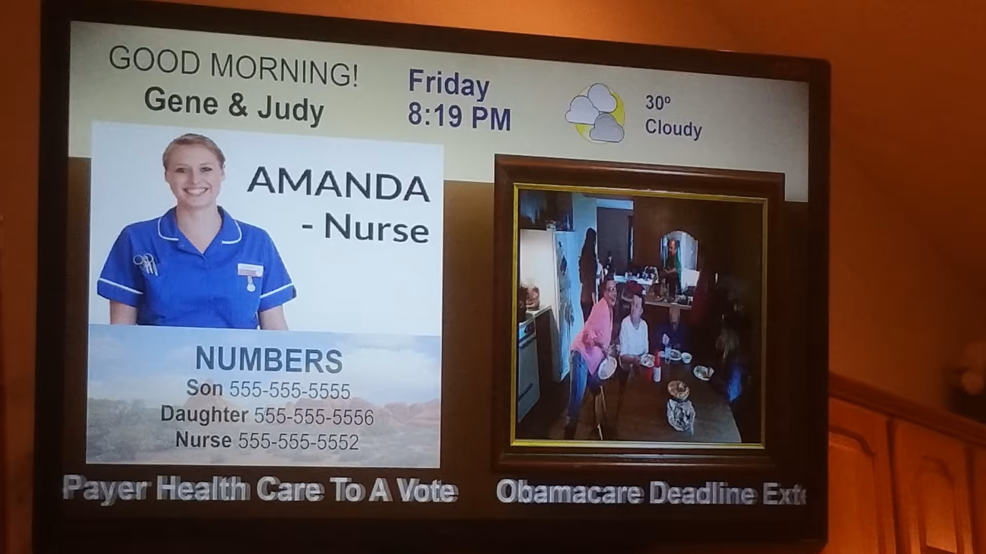 A digital screen displaying a greeting message 'GOOD MORNING! Gene & Judy' with the current day and time as Friday 8:19 PM and weather showing 30 degrees and cloudy. The screen shows a photo of a nurse named Amanda in blue uniform, along with important phone numbers for Son, Daughter, and Nurse. Next to it is a smaller live image of people gathered in a kitchen or dining area. There is a news ticker at the bottom with partial text about healthcare and Obamacare deadline.