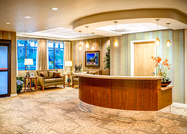 Reception lobby with a curved wooden front desk, pendant lights, seating area with couches and lamps, and framed artwork.