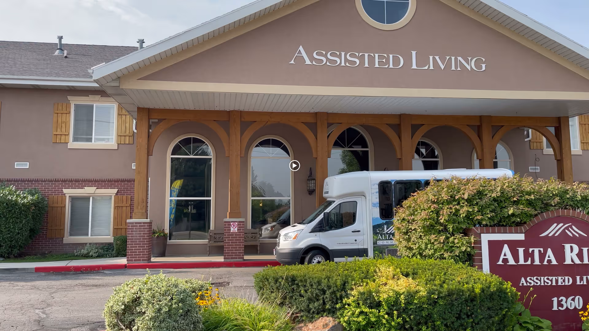 Front entrance of Alta Ridge Assisted Living with a covered portico, shuttle van parked outside and landscaped signage.