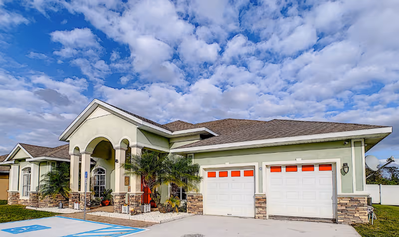 Exterior view of a green assisted living facility with arched entrance and two garage doors.