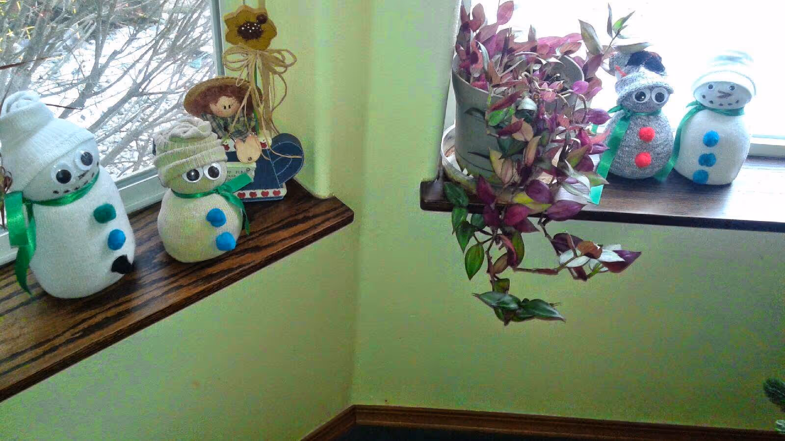 A windowsill decorated with four handmade sock-snowman figures and a trailing potted plant.