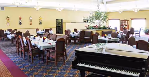 A spacious dining room with white tablecloths, chairs, and a grand piano.