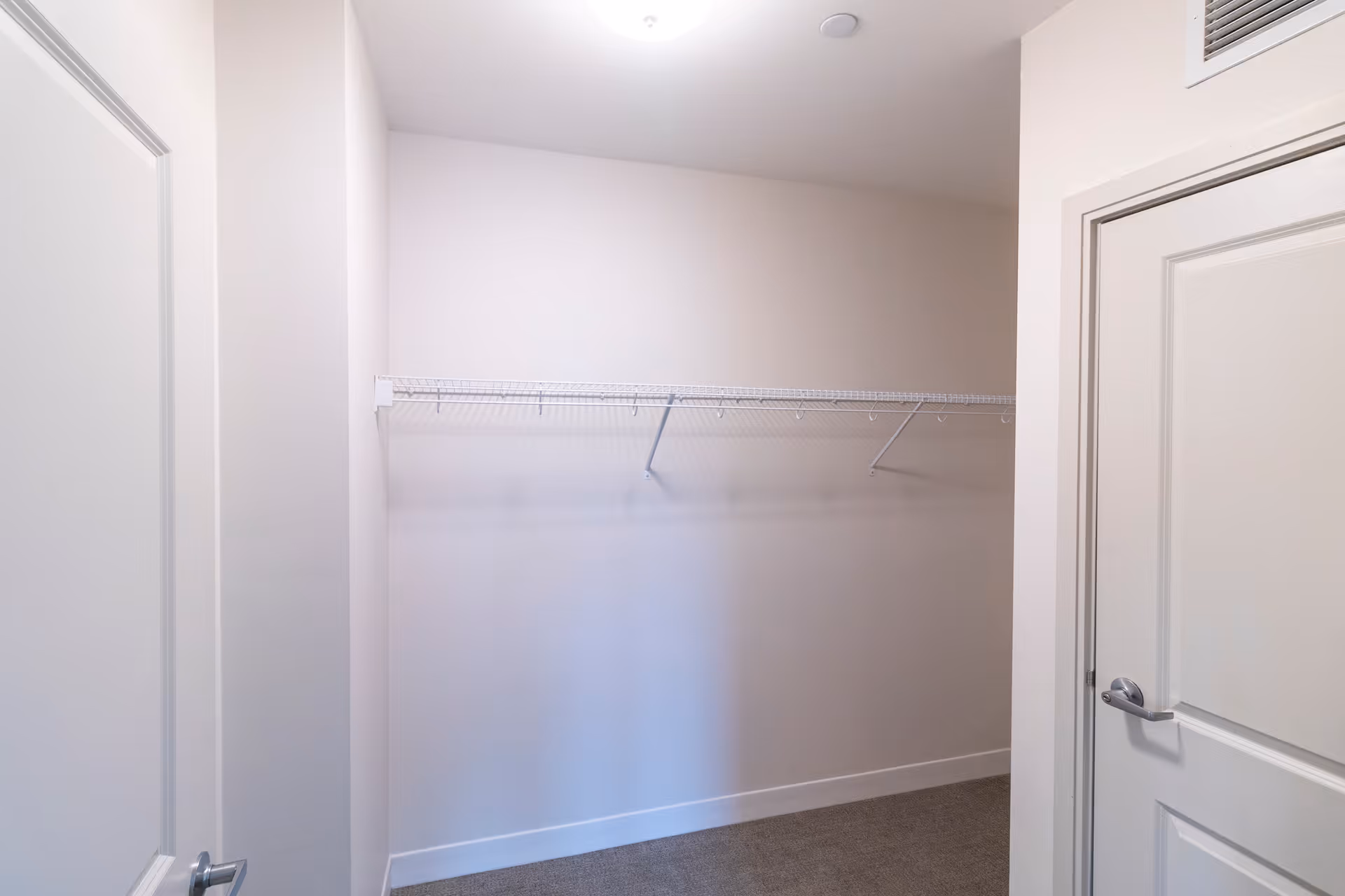 Empty walk-in closet with a single wire shelf and white walls.