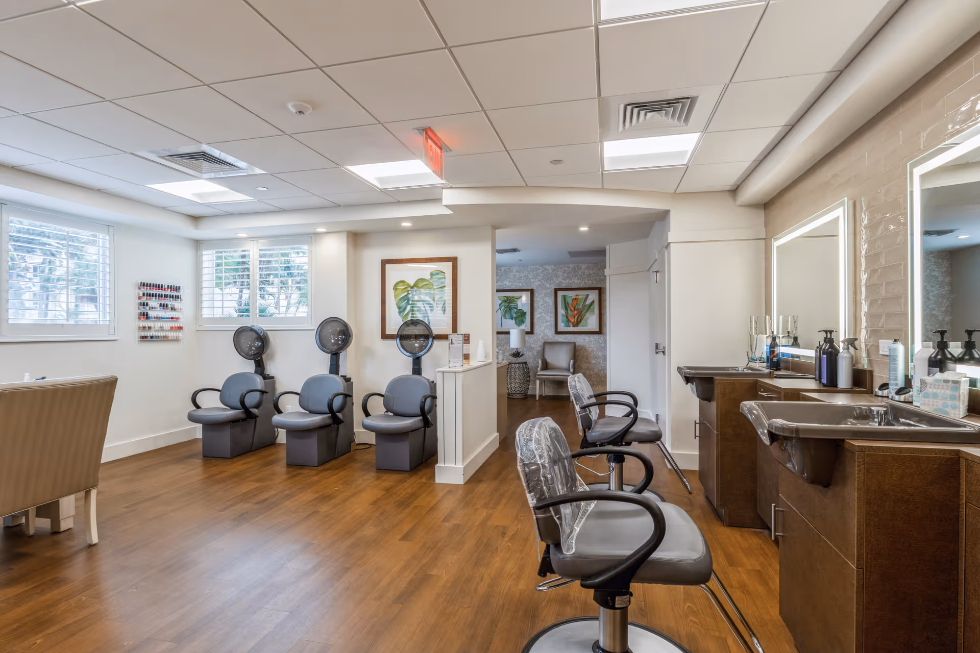 Salon-style common room with hair-styling chairs, hooded dryers, and wash basins in a bright interior.