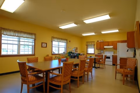 Bright communal dining area with wooden tables and chairs and a small kitchen along the back wall.